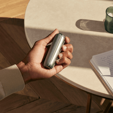 Hand holding Ploom AURA Back Cover Lunar Silver accessory on device.
