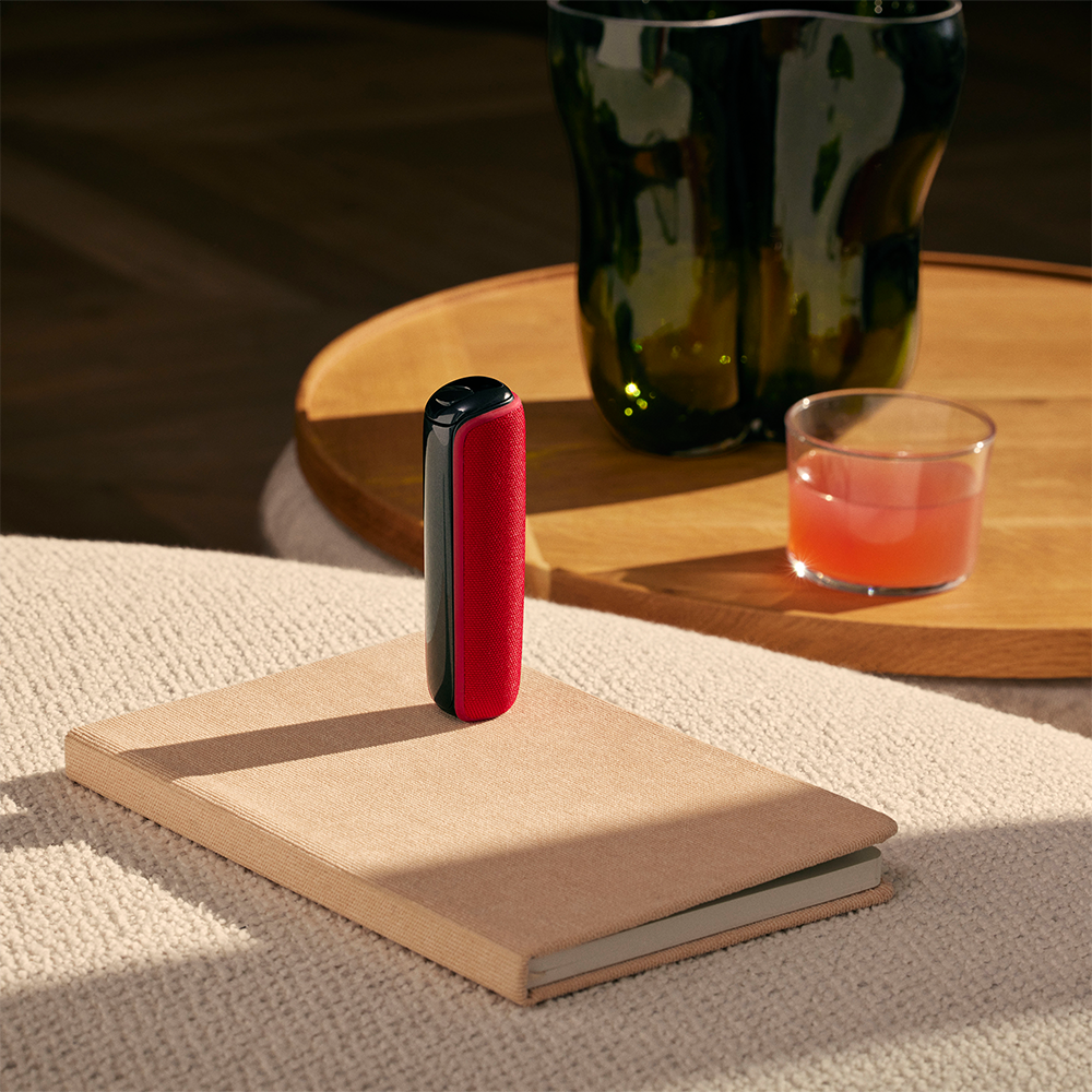 Ploom AURA with Lava Red back cover placed on top of a book on a table.